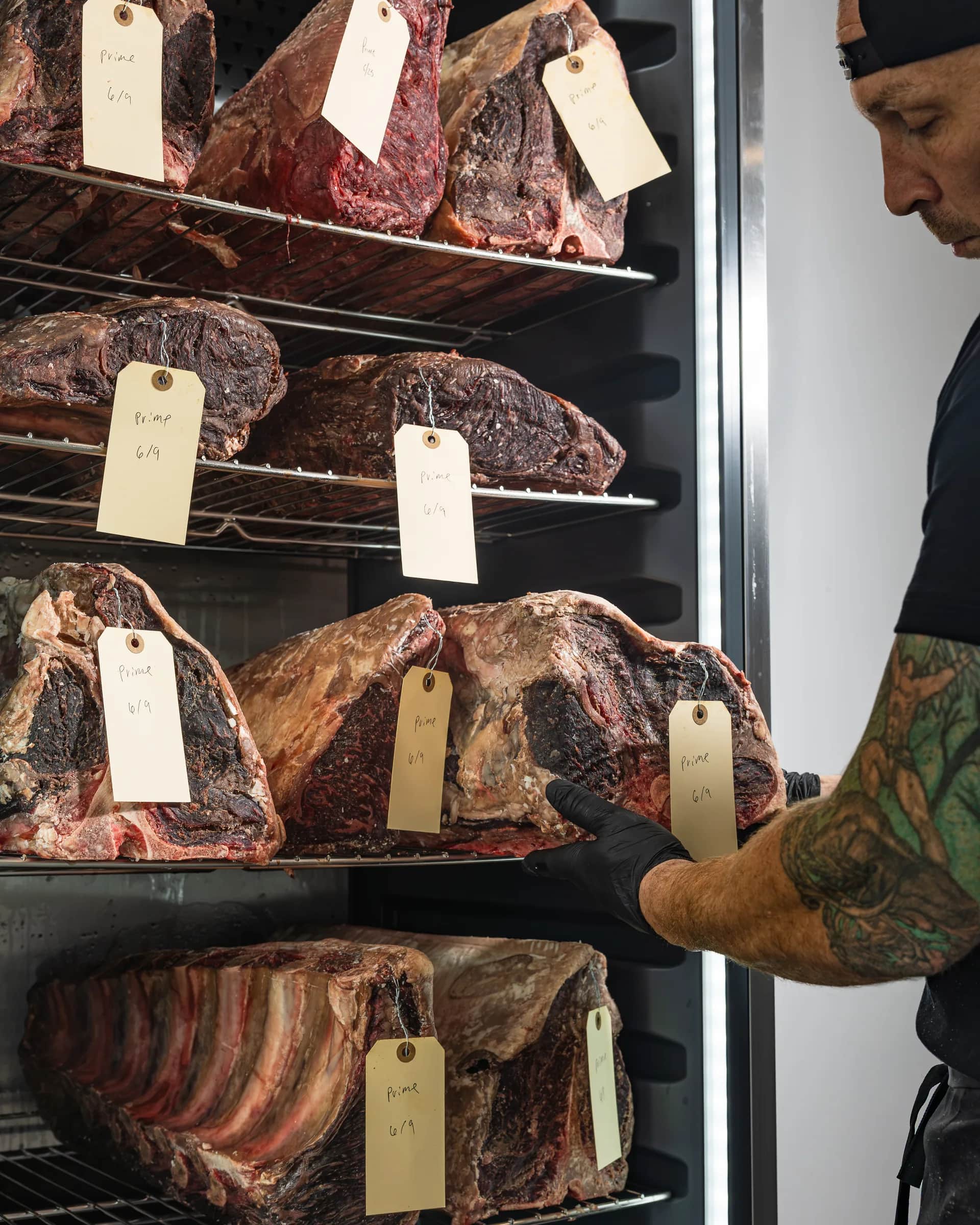 A butcher inspecting whole dry-aged beef primals in the cellar at The Bay Butcher, Oyster Bay, NY