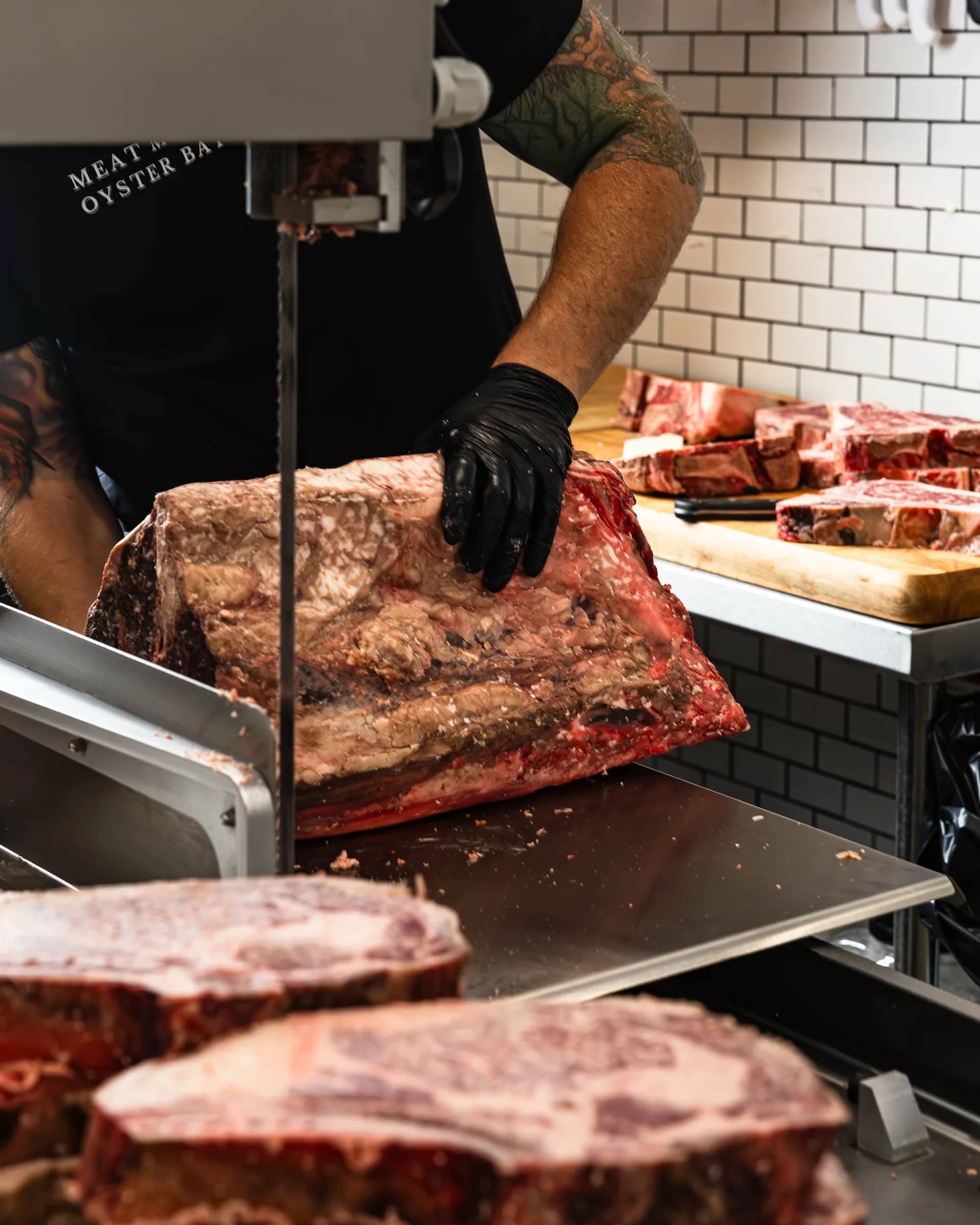 Butcher in a branded apron breaking down a subprimal on the band saw