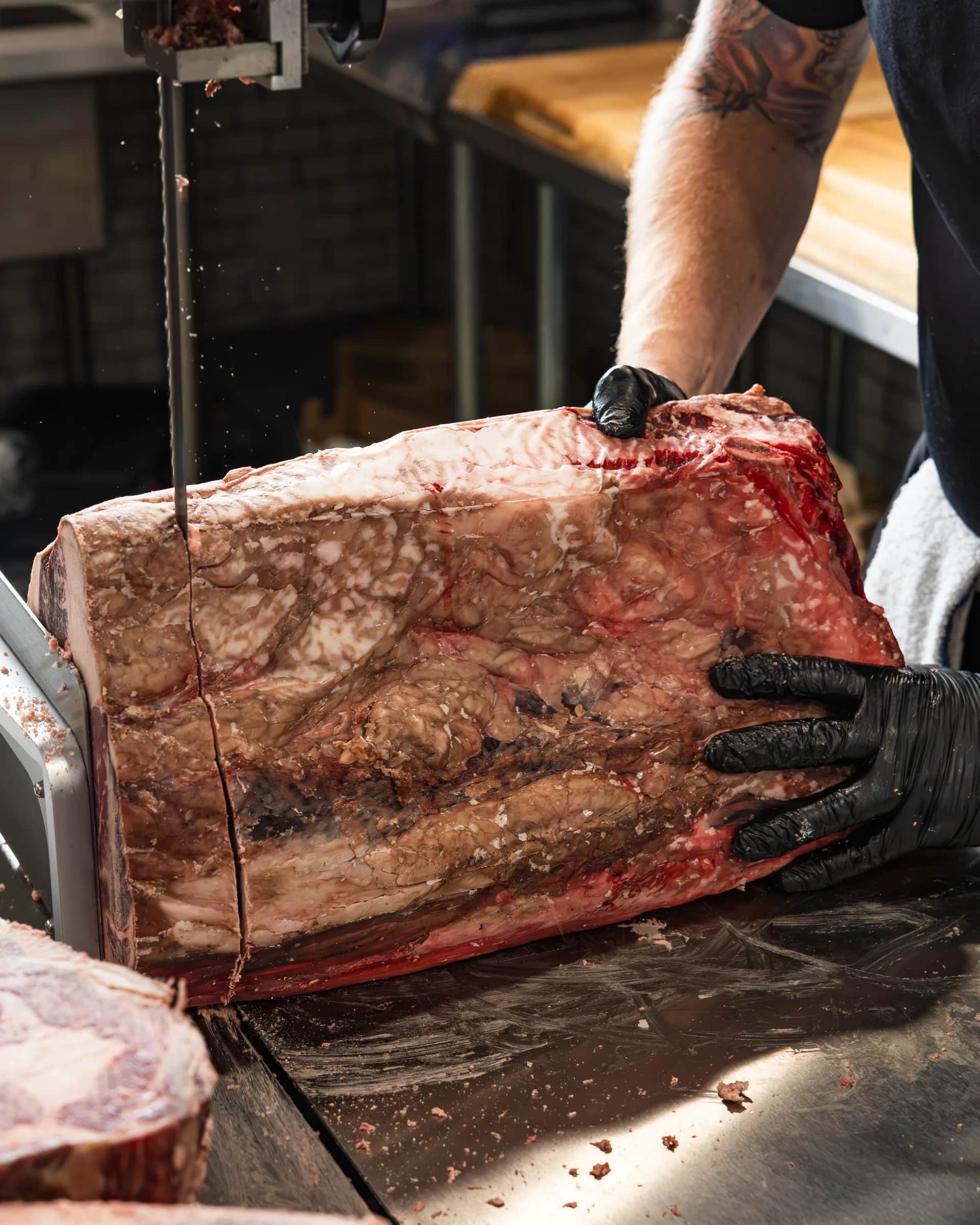 Gloved hands guiding a subprimal through the band saw