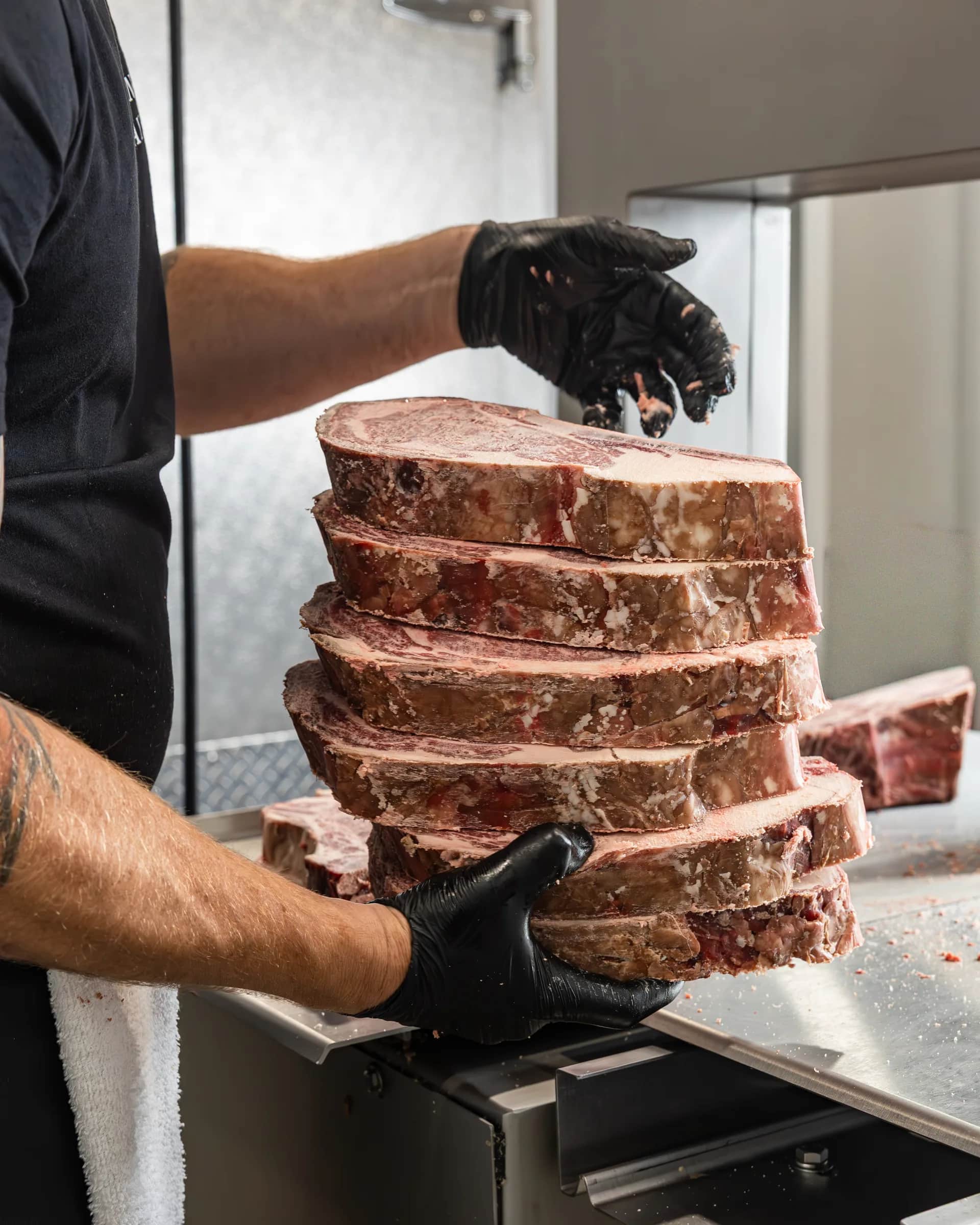 Butcher lifting a tall stack of steaks