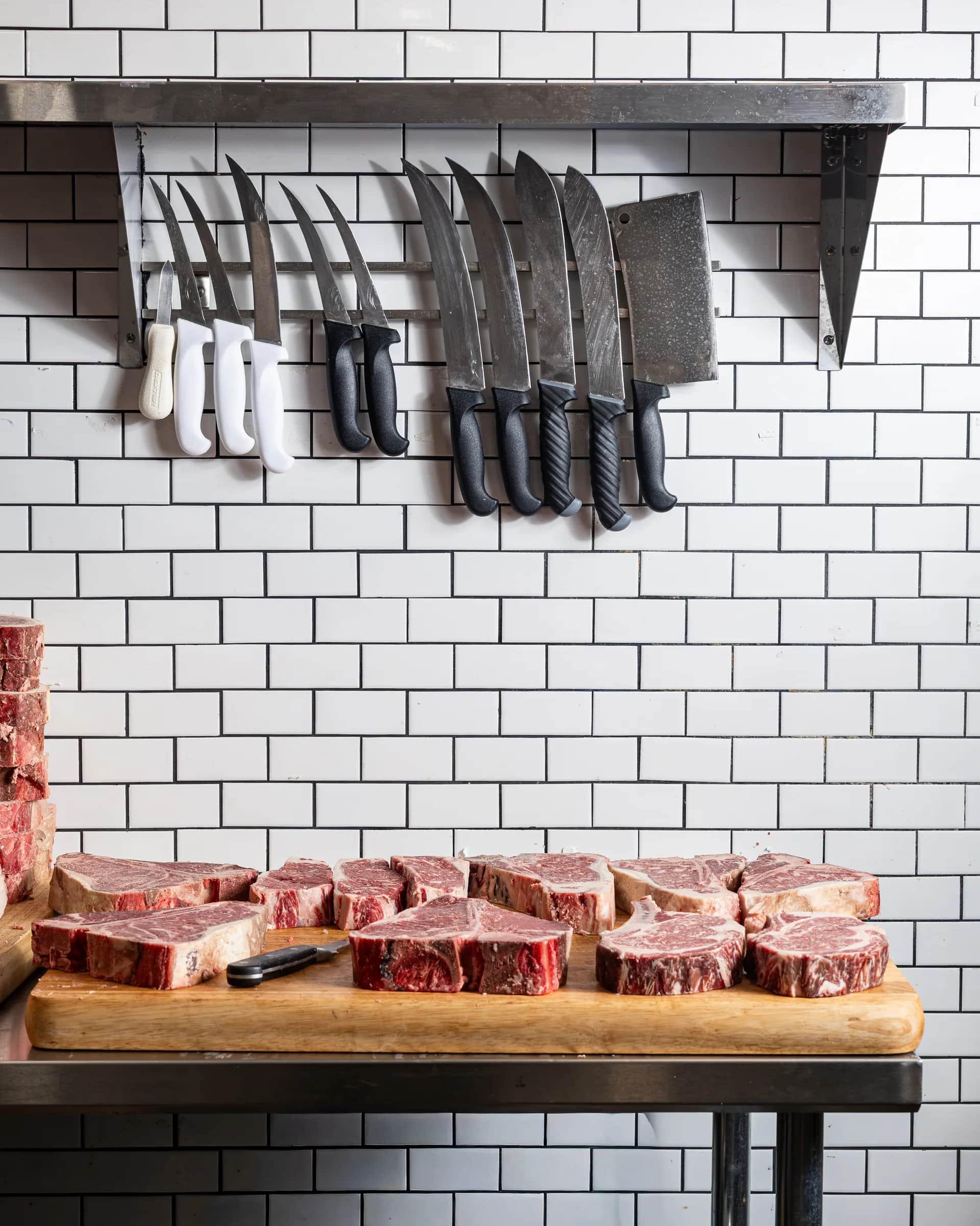 Steaks lined on a wooden board under the knives