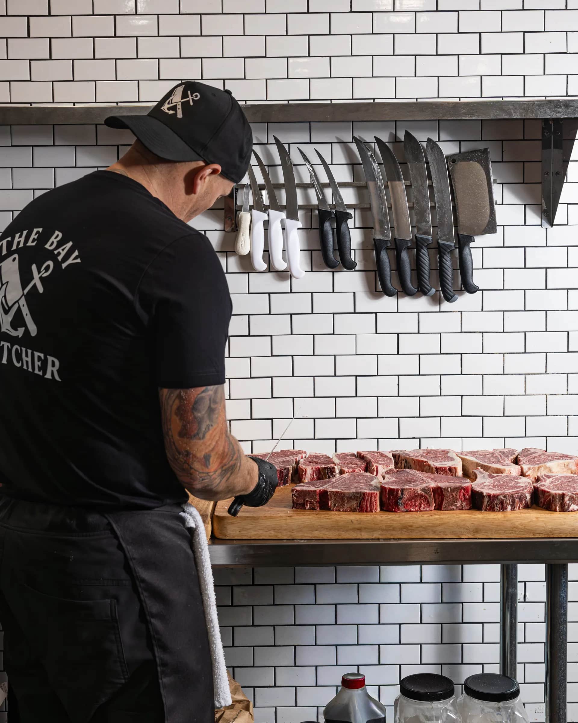 The Bay Butcher tee at the knife wall with a fresh case of steaks